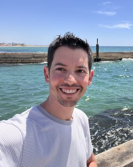 Oded Tsamir on a sea wall, smiling at the camera